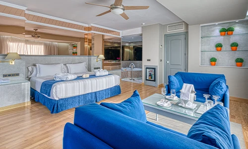 Habitaci&oacute;n moderna con cama, sof&aacute;s azules y mesa con vajilla.