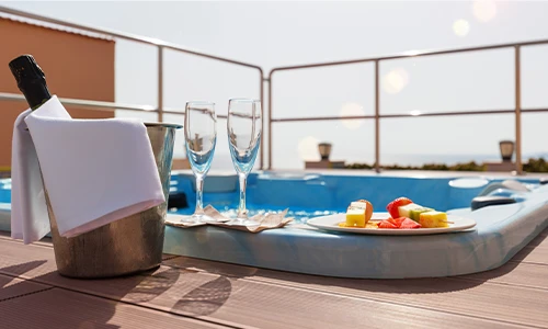 Cubeta con champagne y copas junto a un jacuzzi y plato de frutas.
