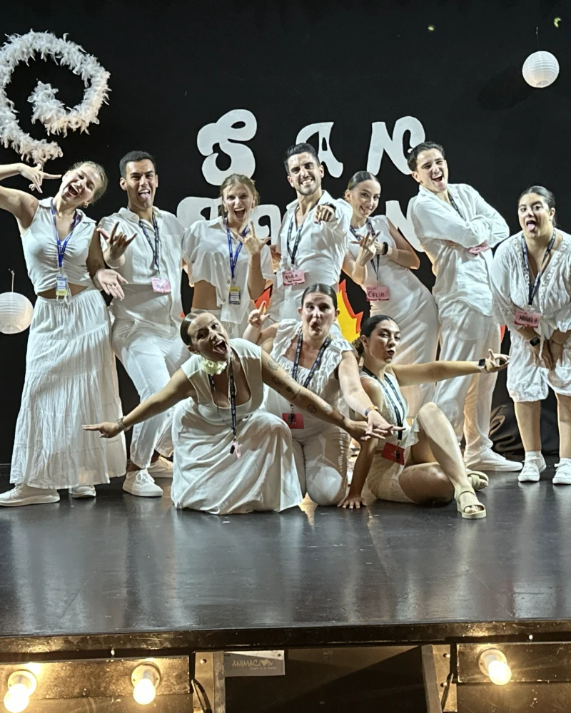 Equipo con trajes blancos y colas, celebrando en escenario con letras y luces