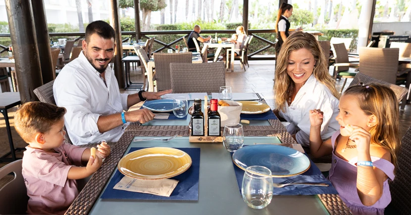 Familia sonriente en restaurante con platos y botellas sobre la mesa