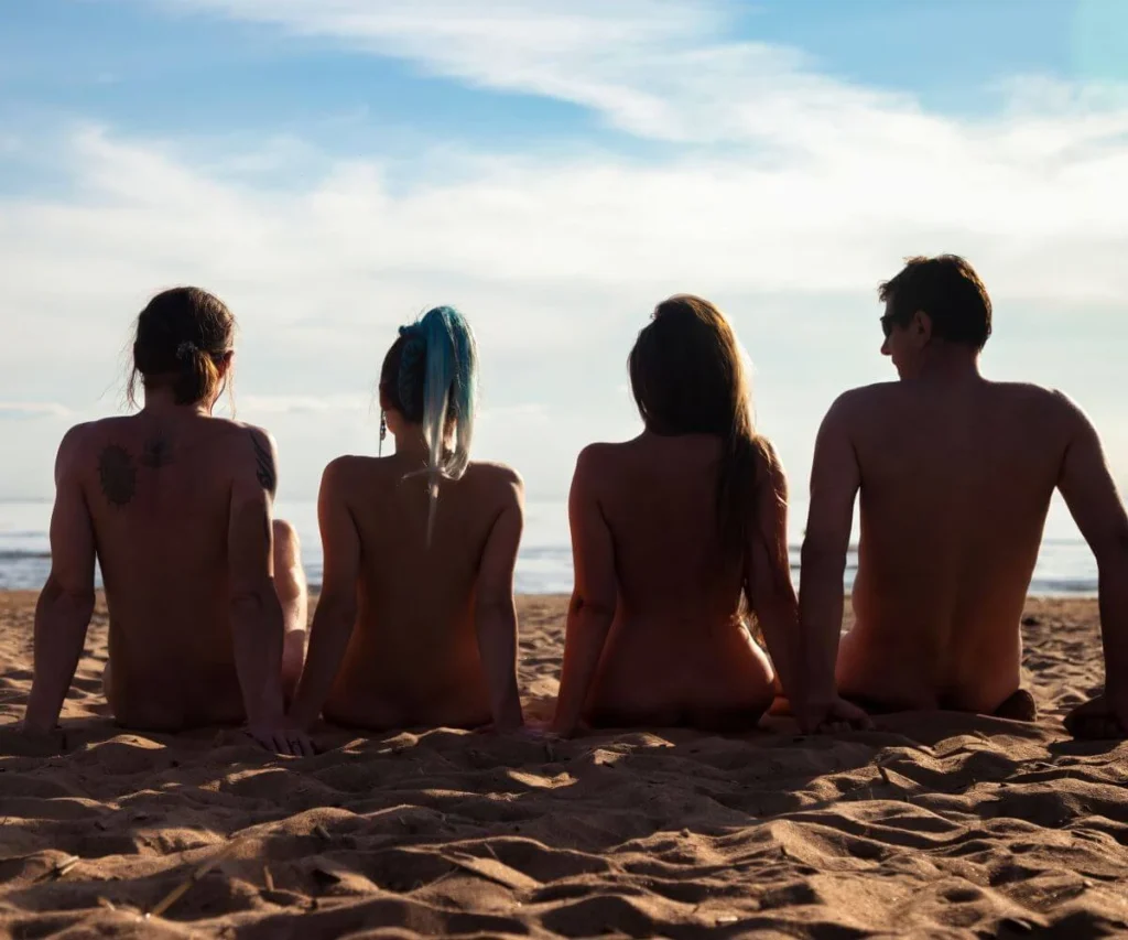 Cuatro personas juntas en la playa, de espaldas, al atardecer