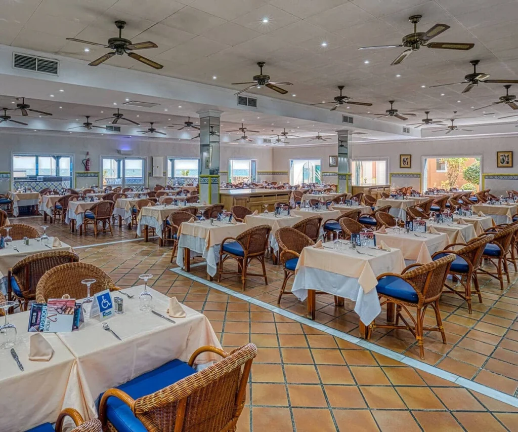 Comedor de hotel con mesas cubiertas, sillas de rat&aacute;n y ventiladores de techo