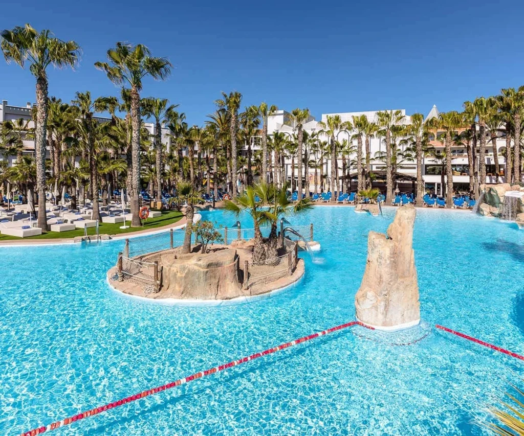 Piscina azul con palmeras y cascada en resort bajo cielo despejado