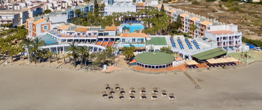 Vista a&eacute;rea de un hotel junto a la playa con piscina y tumbonas azules