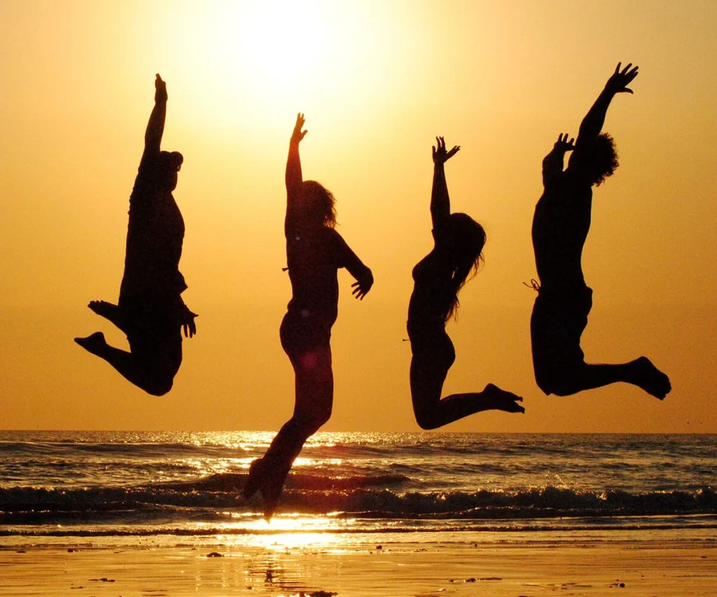 Silhuetas de cuatro personas saltando en la playa al atardecer