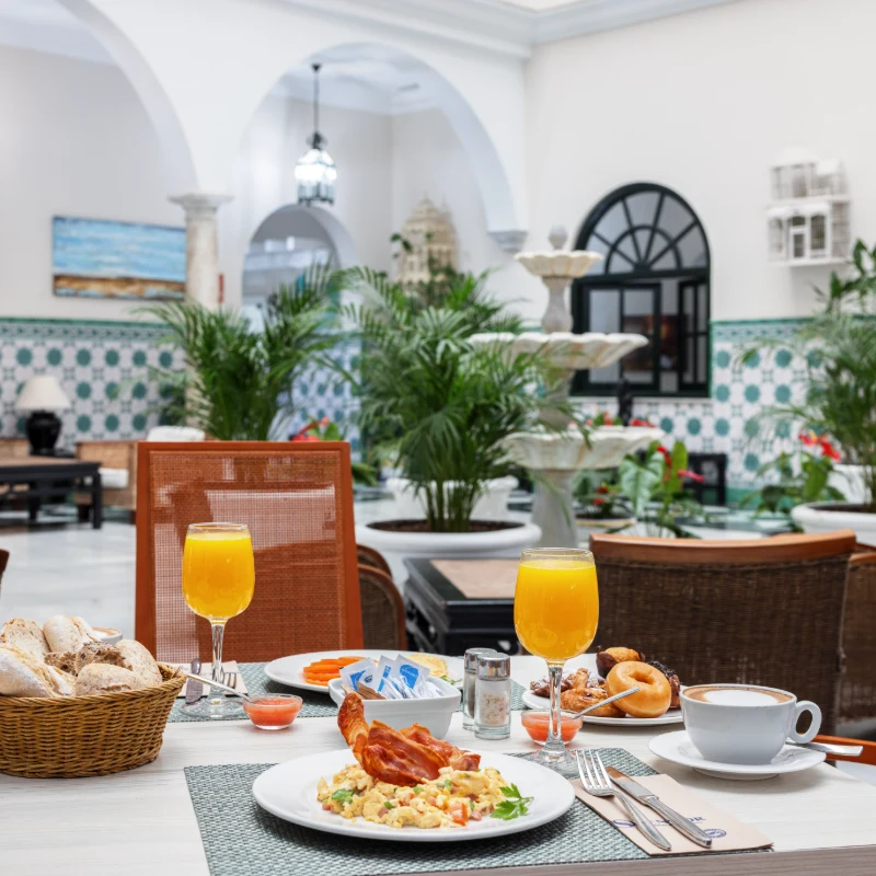 Desayuno servido en un elegante patio interior con plantas y fuente.