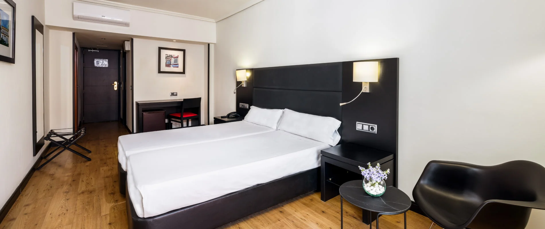 Habitaci&oacute;n de hotel moderna con dos camas, cabecero acolchado y l&aacute;mparas.