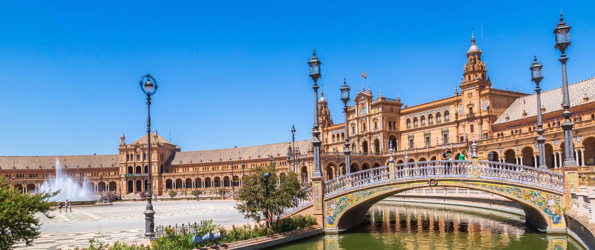 Plaza de Espa&ntilde;a con puente y canal, fuente y edificios hist&oacute;ricos bajo cielo azul.