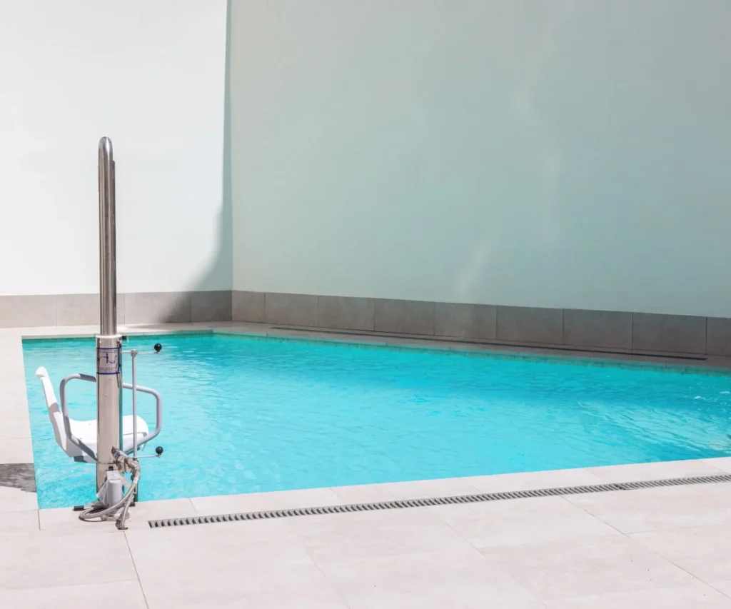 Piscina moderna con agua turquesa, escalera y paredes grises.