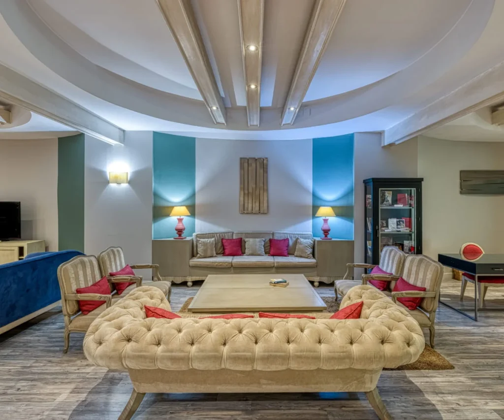 Sala de estar moderna con sillones, sof&aacute; azul y puffs beige, iluminaci&oacute;n LED.