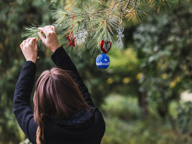 Señora poniendo decoración de navidad en un árbol natural
