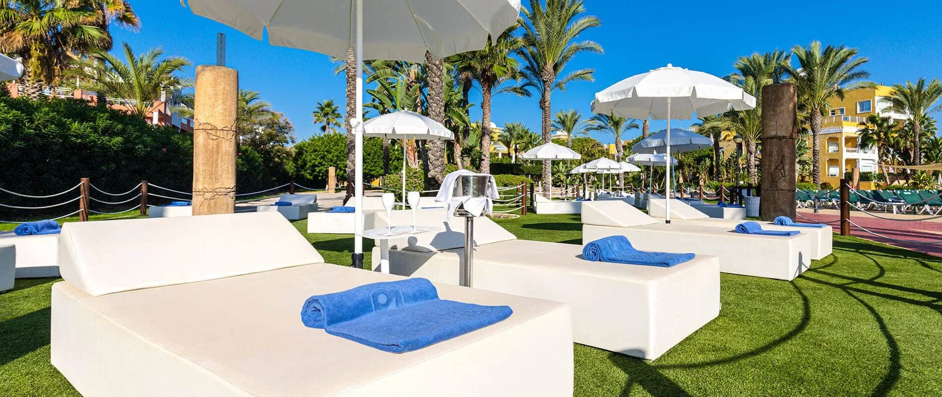 Terraza con tumbonas blancas y sombrillas en jard&iacute;n tropical, junto a piscina