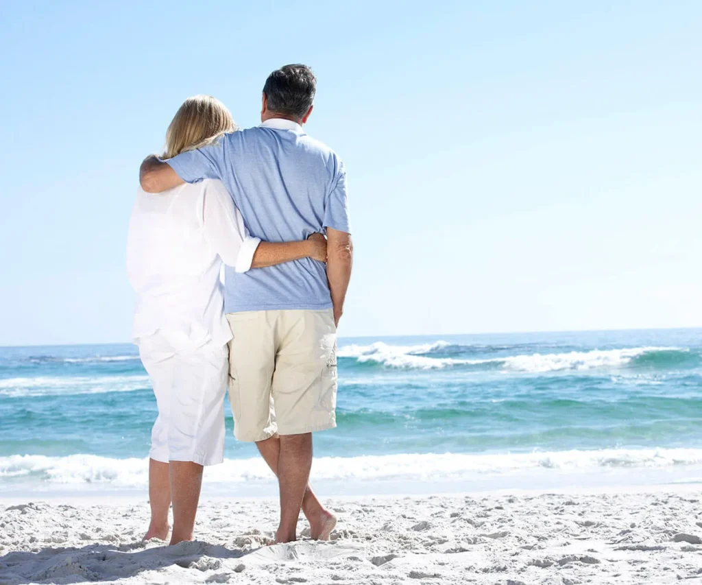 Pareja abrazada en la playa, de espaldas, con el mar y cielo despejado