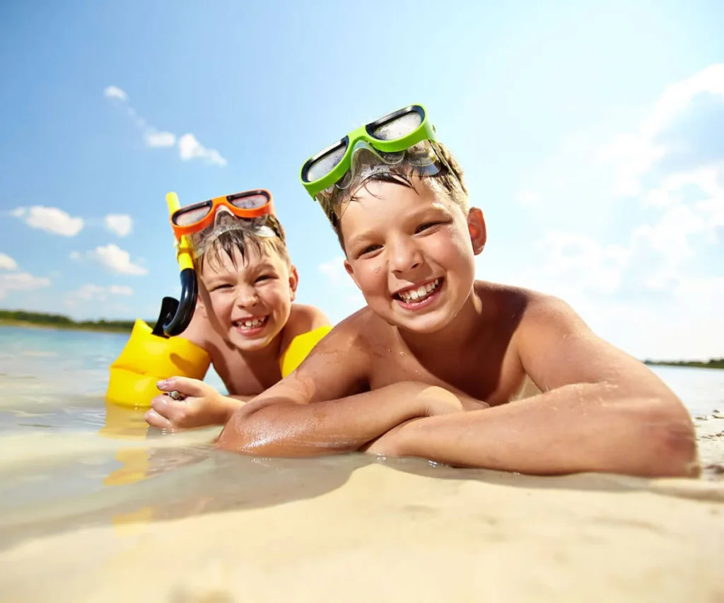 Dos ni&ntilde;os nadan en la playa con aletas y gafas de buceo, sonriendo