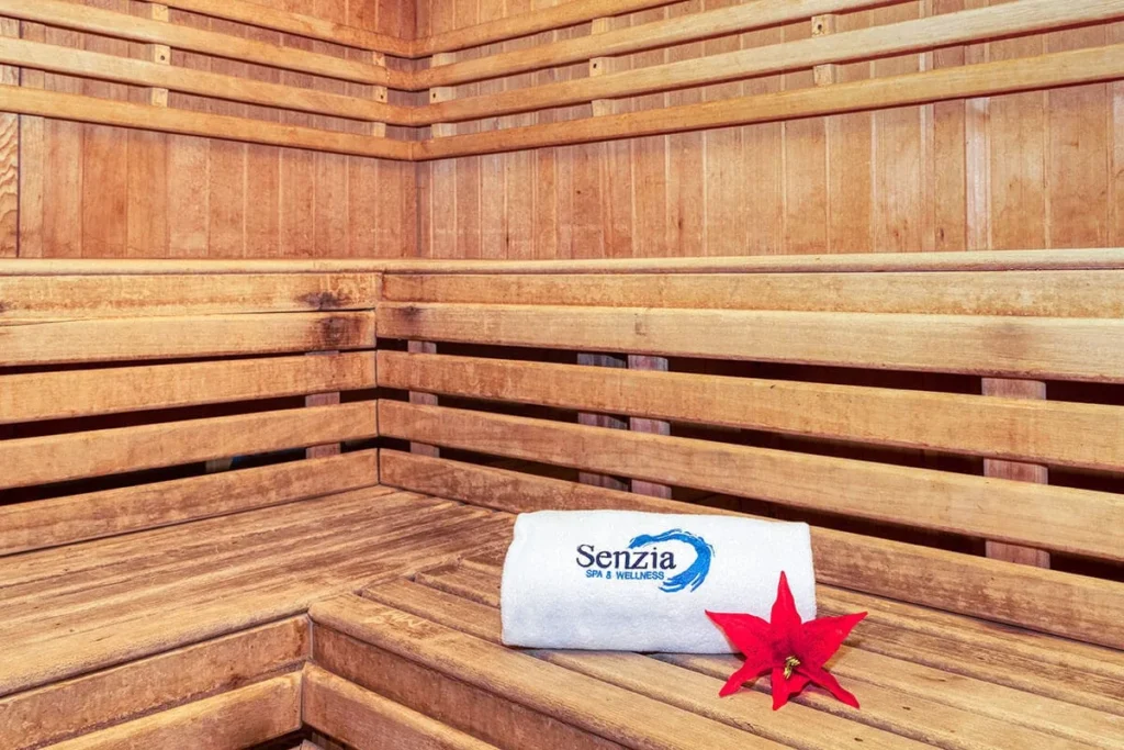 Interior de sauna de madera con toalla Senziа y flor roja sobre el banco