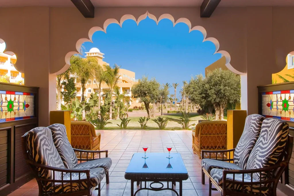 Terraza interior con mesa y dos copas, vista a jard&iacute;n con palmeras y cielo azul