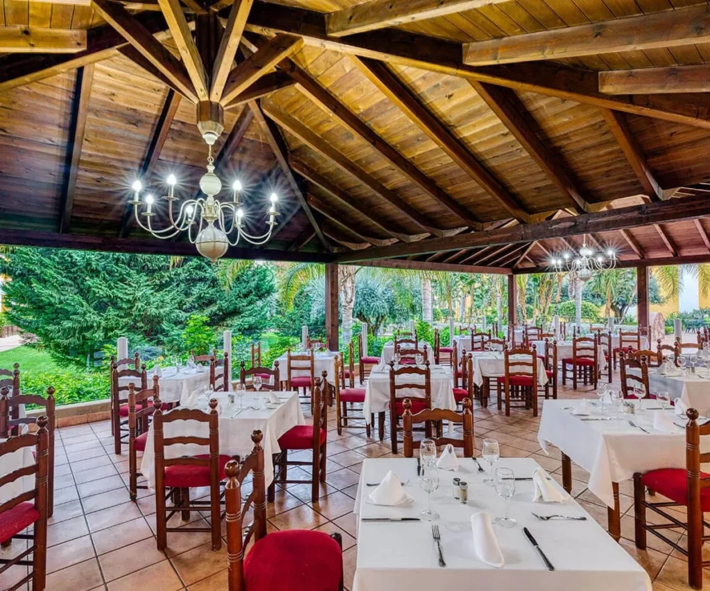 Comedor con mesas y sillas rojas, techo de madera y candelabros en jard&iacute;n