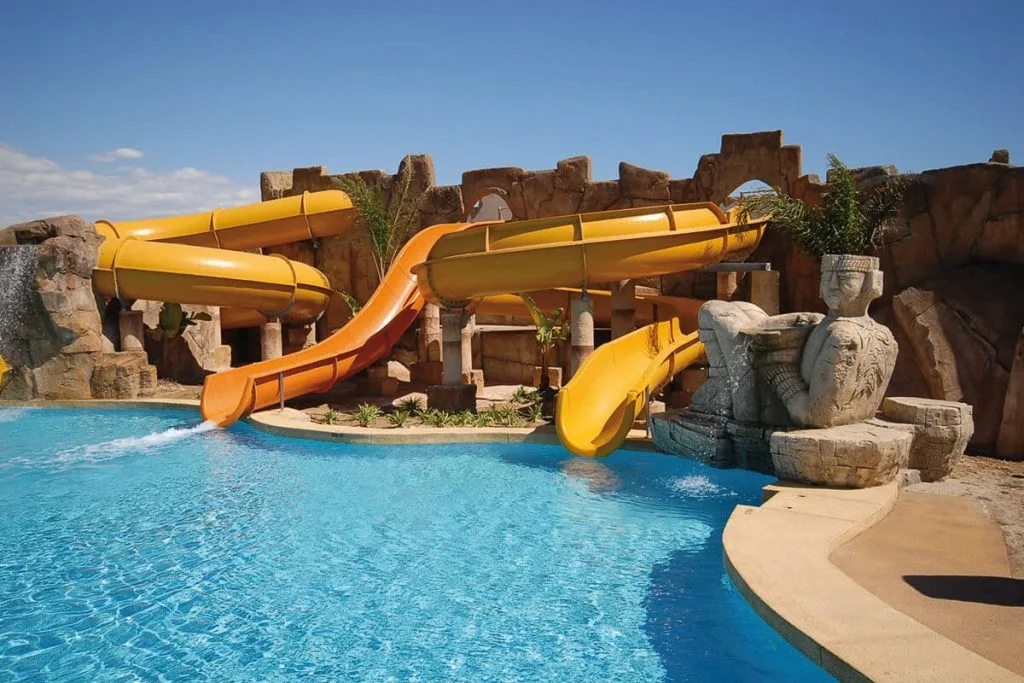 Piscina con toboganes amarillos y figuras de piedra en un parque acu&aacute;tico