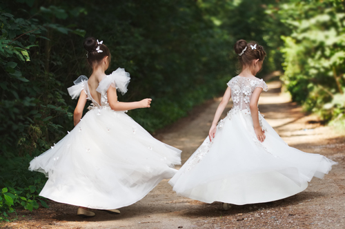 Dos niñas con vestidos blancos giran alegremente en un camino rodeado de vegetación.