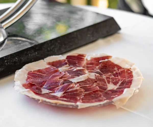 Plato de jamón ibérico cortado en finas lonchas sobre una mesa blanca.