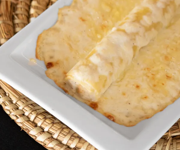 Plato de canelón con salsa blanca en una bandeja sobre un mantel tejido.