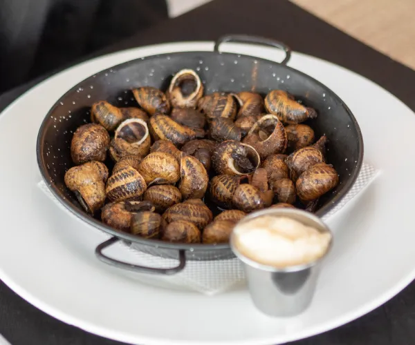 Plato negro con caracoles cocidos y salsa en un recipiente pequeño aparte.