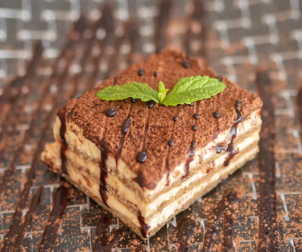 Tiramisú decorado con menta y salsa de chocolate sobre plato marrón.