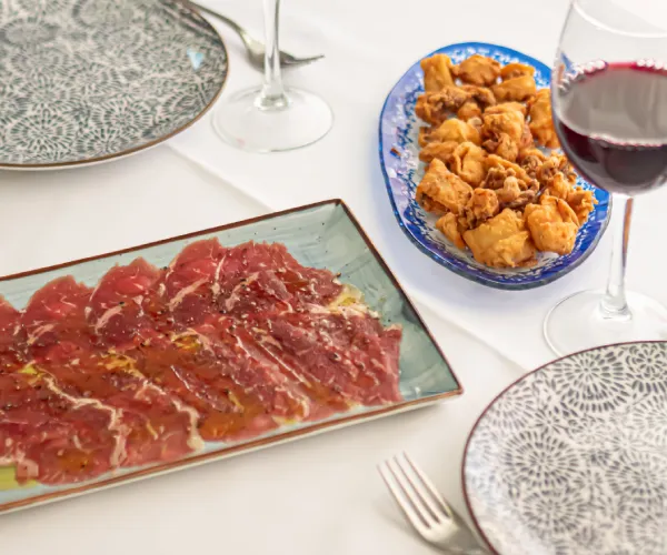 Platos de embutidos y fritos con una copa de vino tinto sobre la mesa.