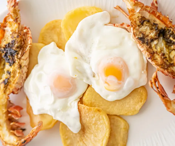 Huevos fritos sobre patatas con colas de langosta.
