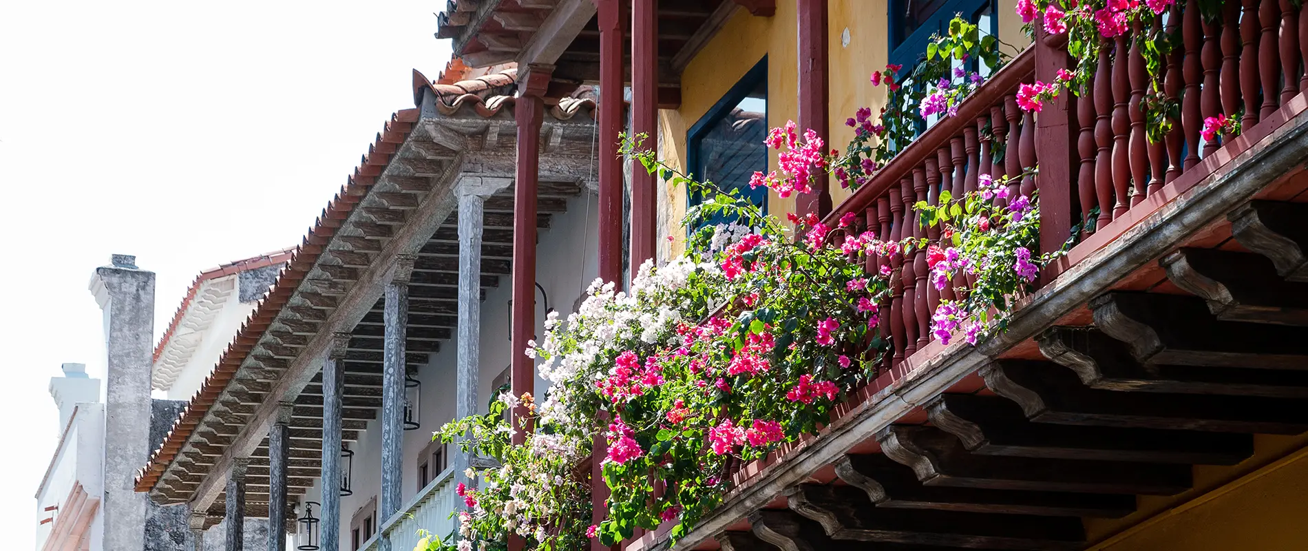 Balcones de madera adornados con flores de colores vibrantes, sobre una fachada amarilla en un estilo colonial.