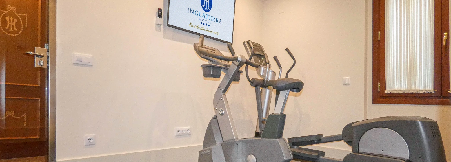 Bicicleta el&iacute;ptica y panel con el logo del Hotel Inglaterra en un gimnasio
