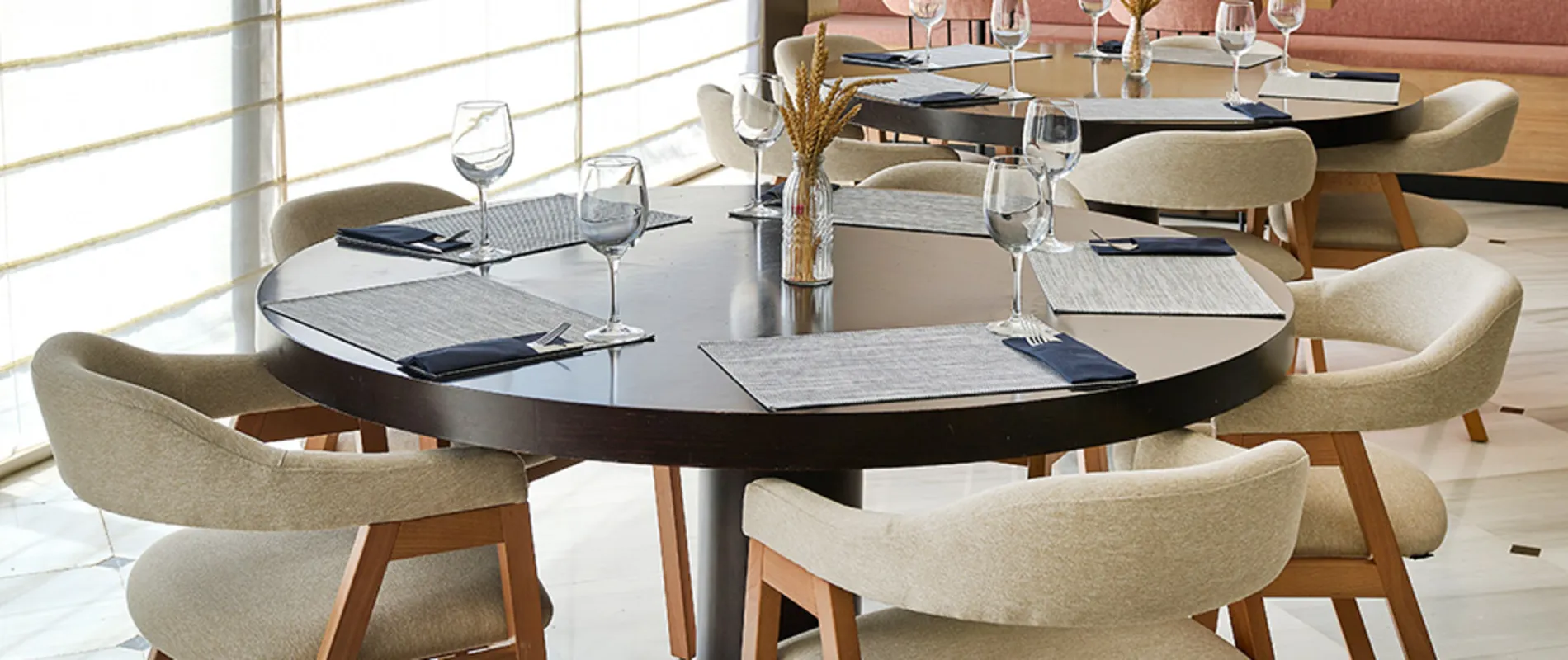 Mesa redonda con vajilla y copas en un comedor moderno, junto a ventanales