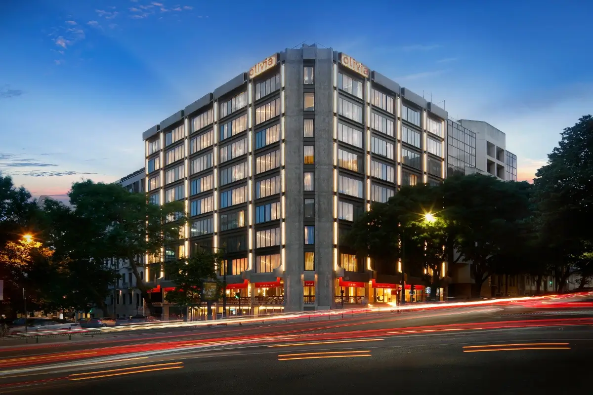 Edificio de oficinas con letrero “Oliva” al atardecer y luces de vehículos.