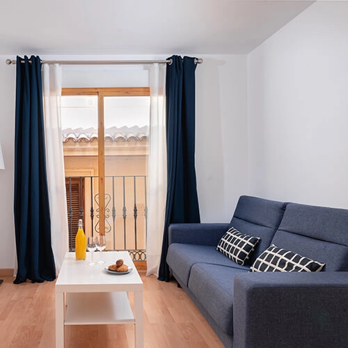 Sala con sof&aacute; azul, mesa blanca, ventana y cortinas navy.