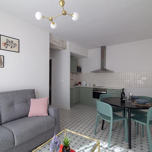 Sala y cocina modernas, sof&aacute; gris, mesa redonda y l&aacute;mpara de techo.