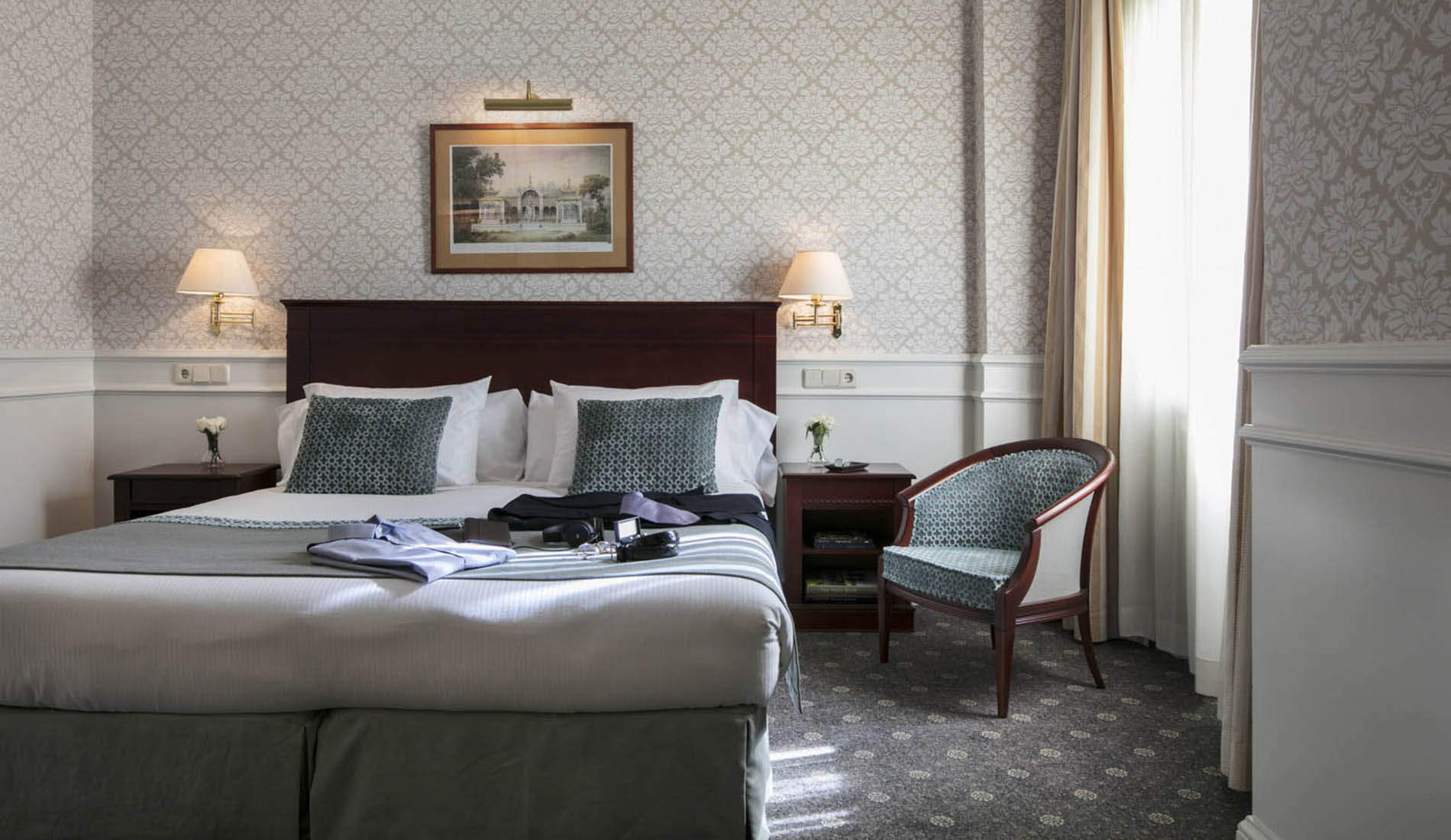 Habitación de hotel elegante con cama doble y silla junto a una ventana iluminada.