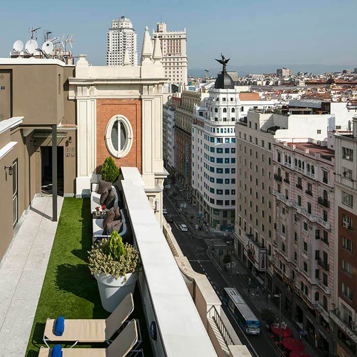 Vista de una azotea con sillones y plantas, y una calle concurrida en la ciudad al fondo.