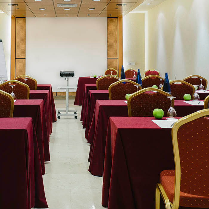 Sala de conferencias vacía con mesas cubiertas de manteles rojos y sillas alineadas.