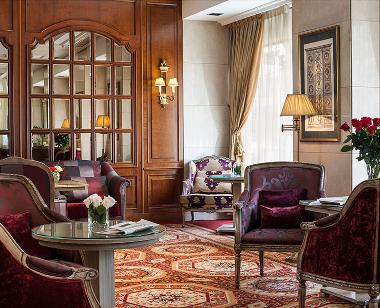 Sala elegante con sillones de terciopelo, alfombra roja y una lámpara junto a cortinas doradas.