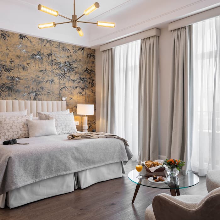 Habitación elegante con cama, lámpara moderna y mesa con desayuno. Pared decorada con bambú.