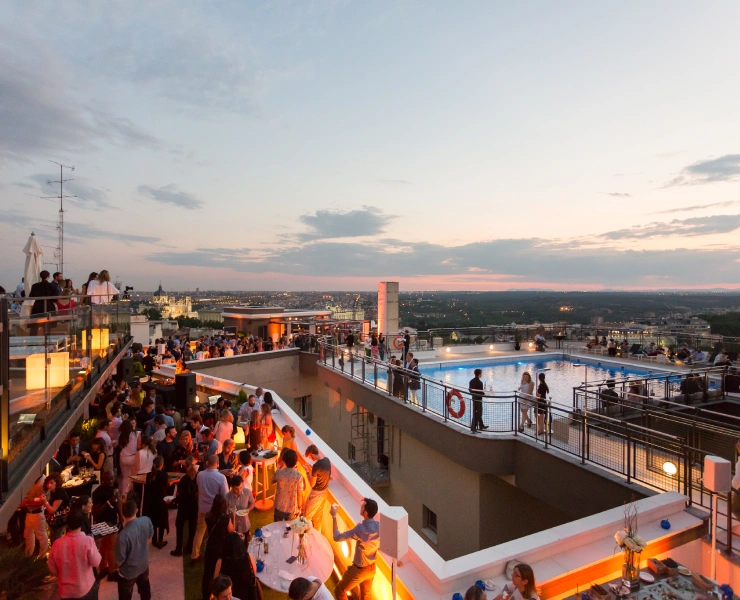 Fiesta en una azotea al atardecer, con piscina y vista panorámica de la ciudad.