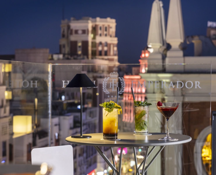 Cócteles sobre una mesa en una terraza con vistas a una ciudad iluminada por la noche.