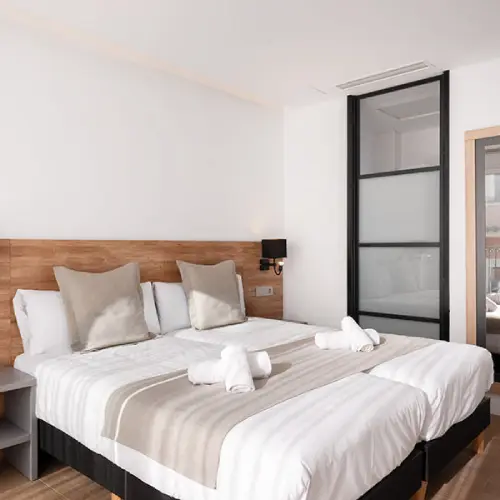 Habitaci&oacute;n moderna con dos camas juntas, decoraci&oacute;n minimalista y toallas blancas.